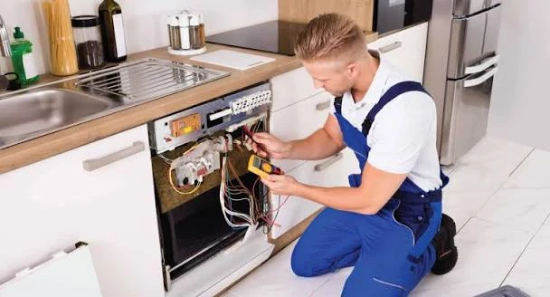 Technician checking dishwasher wiring and controls beneath a kitchen counter