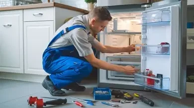 Technician inspecting the interior of an open refrigerator with tools nearby